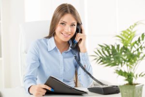 Young business woman phoning in office sitting at an office desk with one hand holding the phone and in another folder.
